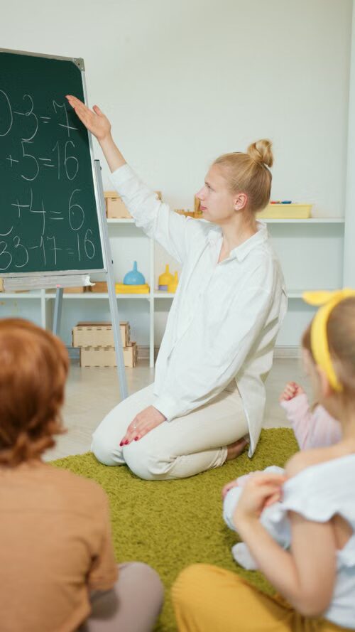Enseignante au tableau avec un groupe d’enfants assis au sol